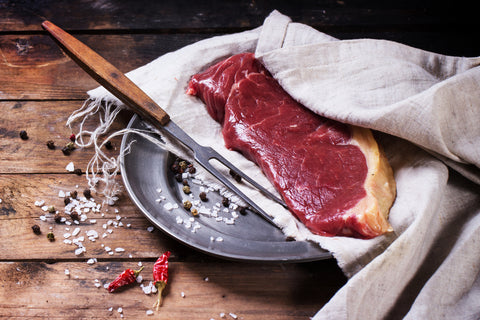 Raw grass-fed beef steak on a metal plate with coarse salt and pepper on a rustic wooden table